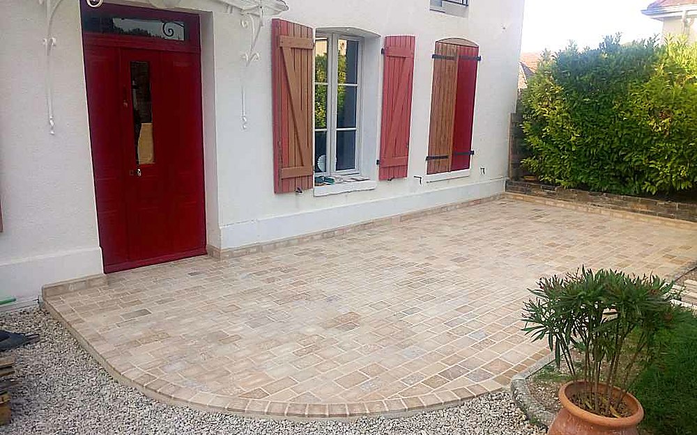 Terrasse en pavés de Bourgogne devant une maison à porte et volets rouges
