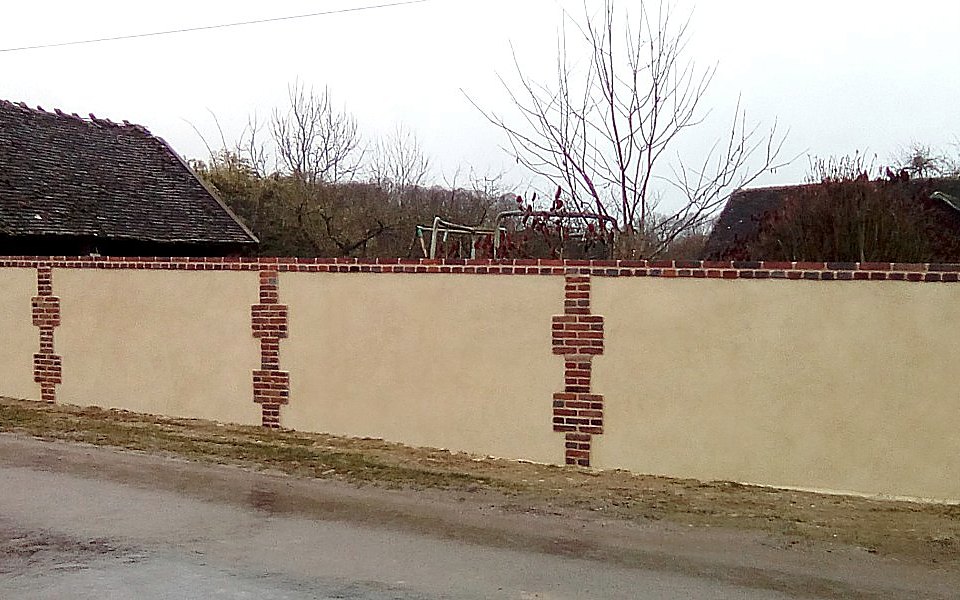 Mur de clôture enduit rythmé de chaînes verticales en briques, refait au style ancien